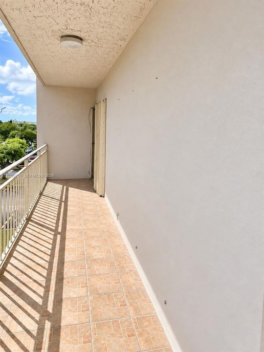 Covered outdoor balcony featuring neutral tile flooring, a painted textured ceiling with a flush-mount light fixture, and white metal railings