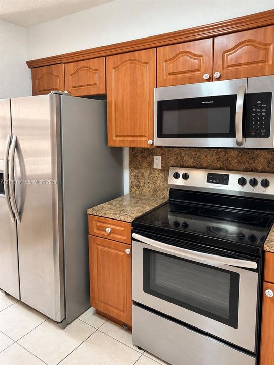 Kitchen featuring wood cabinetry, stainless steel refrigerator, stainless steel over-the-range microwave, stainless steel electric range, and stone-patterned laminate countertops