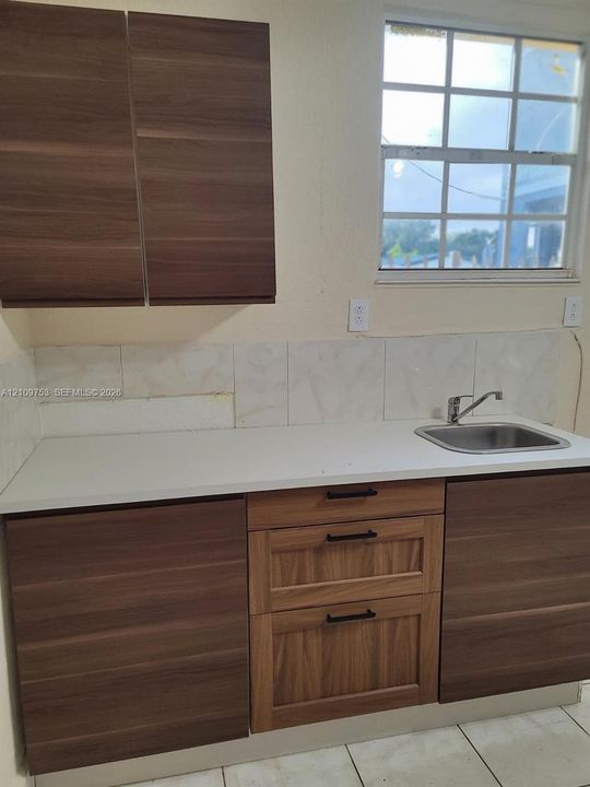 Kitchen featuring wood-finish cabinetry, solid surface countertop, stainless steel sink with metal faucet, and grid-patterned window