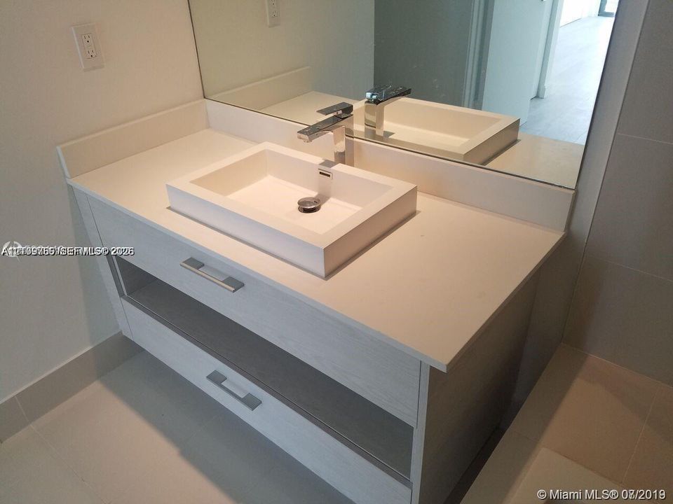 Modern floating vanity with a light wood-finish frame, rectangular vessel sink, solid-surface countertop, and polished chrome faucet