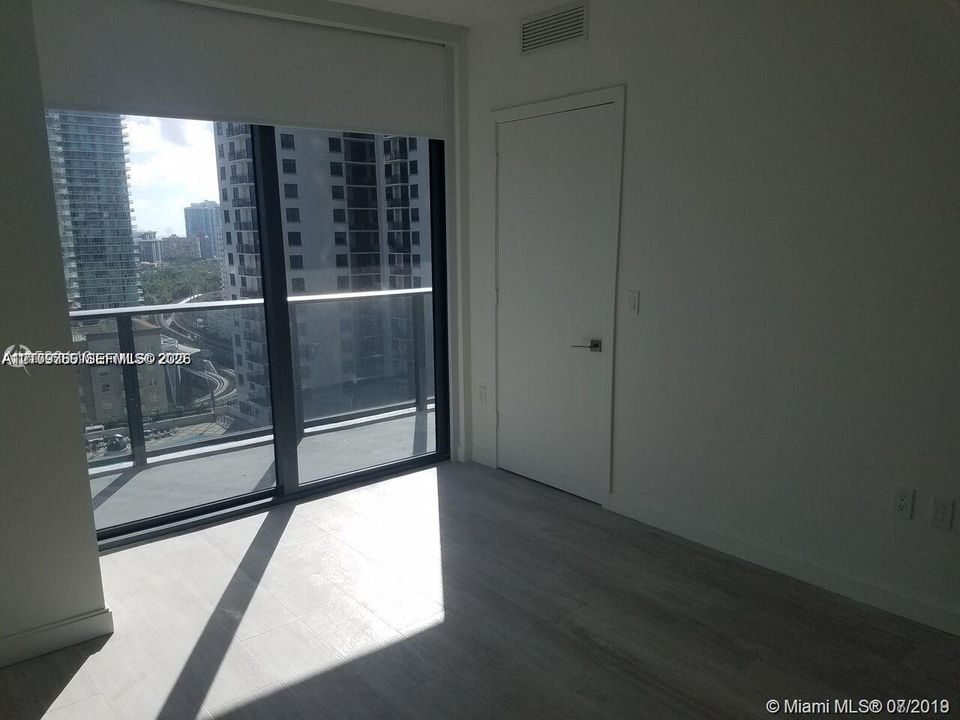 Floor-to-ceiling glass wall, private balcony with metal railing, and neutral tile flooring throughout