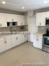 Kitchen featuring white shaker-style cabinetry, solid-surface countertops, recessed lighting, and stainless steel appliances