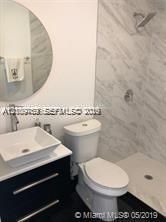 Modern floating vanity with a white vessel sink, quartz countertop, polished chrome faucet, round mirror, and a walk-in shower with stone-finish tile surround