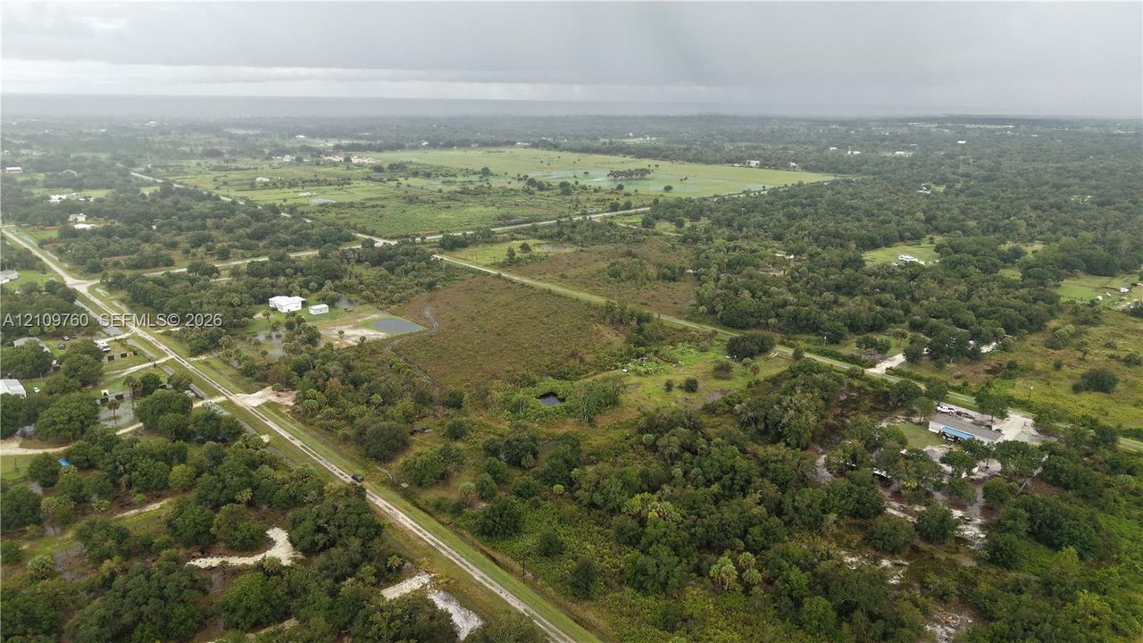 Aerial perspective of expansive acreage featuring mature tree clusters, open meadow space, and paved road access