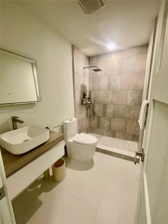 Floating vanity with a rectangular vessel sink and wood-finish countertop, walk-in shower featuring large-format wall tile, hexagonal floor tile, and a rainfall showerhead