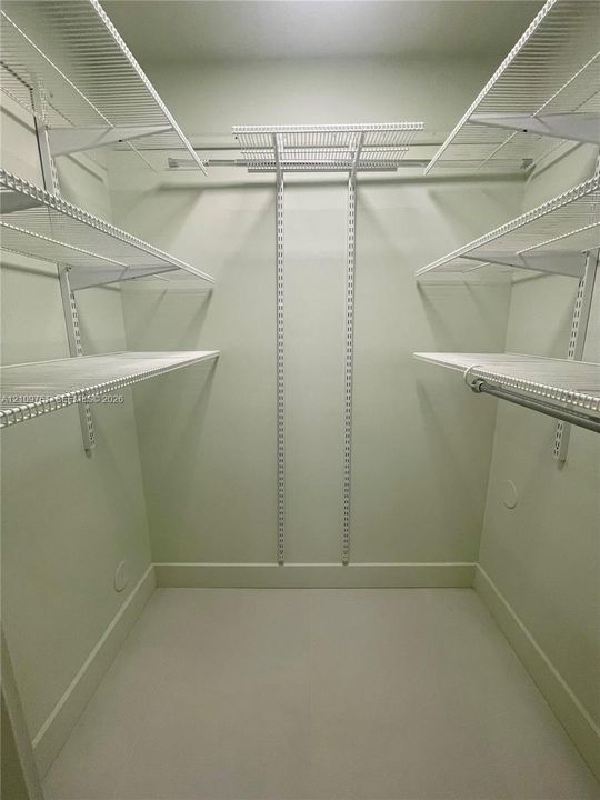 Walk-in closet featuring tiered white wire shelving, adjustable wall-mounted support tracks, and integrated hanging rods