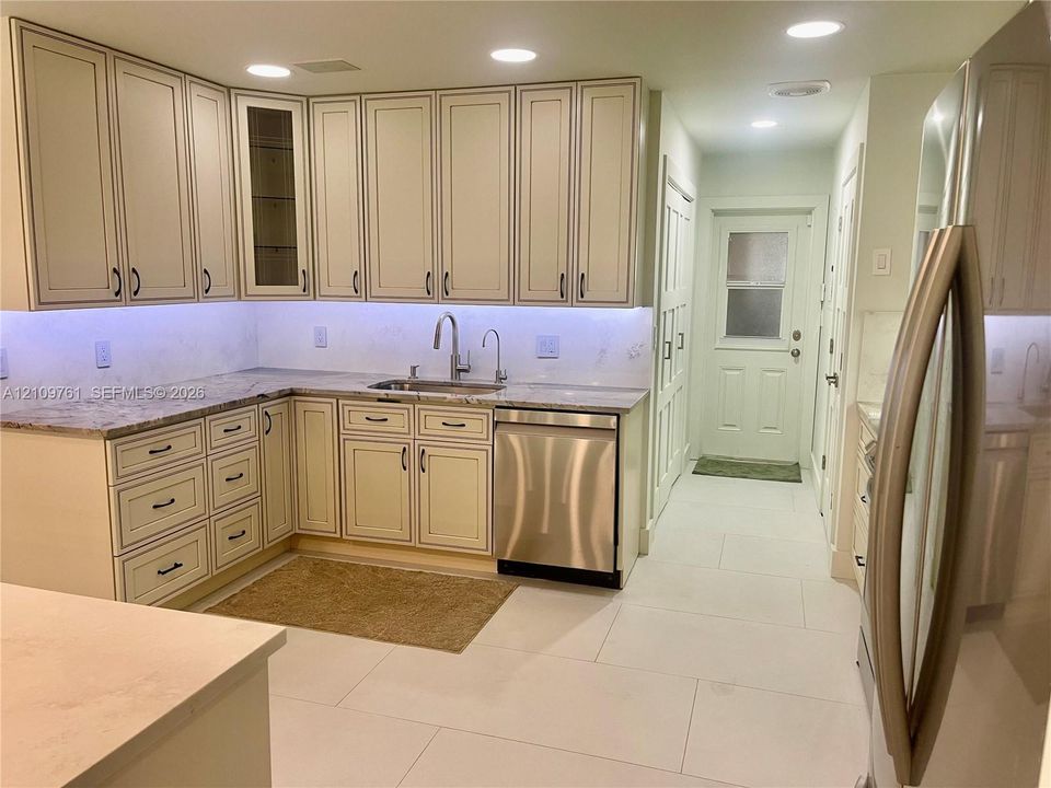 Kitchen featuring shaker-style cabinetry with integrated glass-front doors, stone countertops, stainless steel dishwasher, undermount sink with gooseneck faucet, and porcelain tile flooring