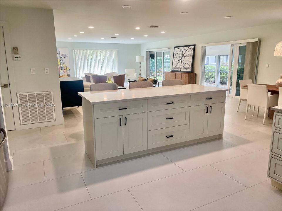 Oversized kitchen island with solid-surface countertops, shaker-style cabinetry, matte black hardware, and large-format tile flooring