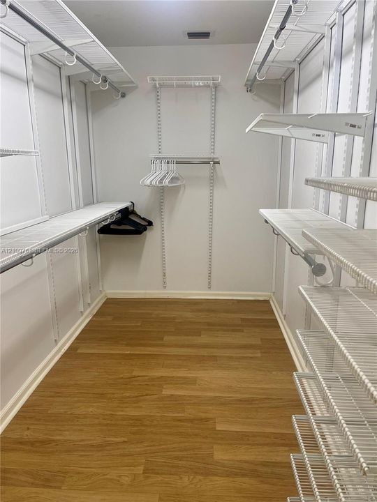 Walk-in closet featuring wood-finish flooring and integrated white wire shelving systems with multiple hanging rods and tiered storage racks