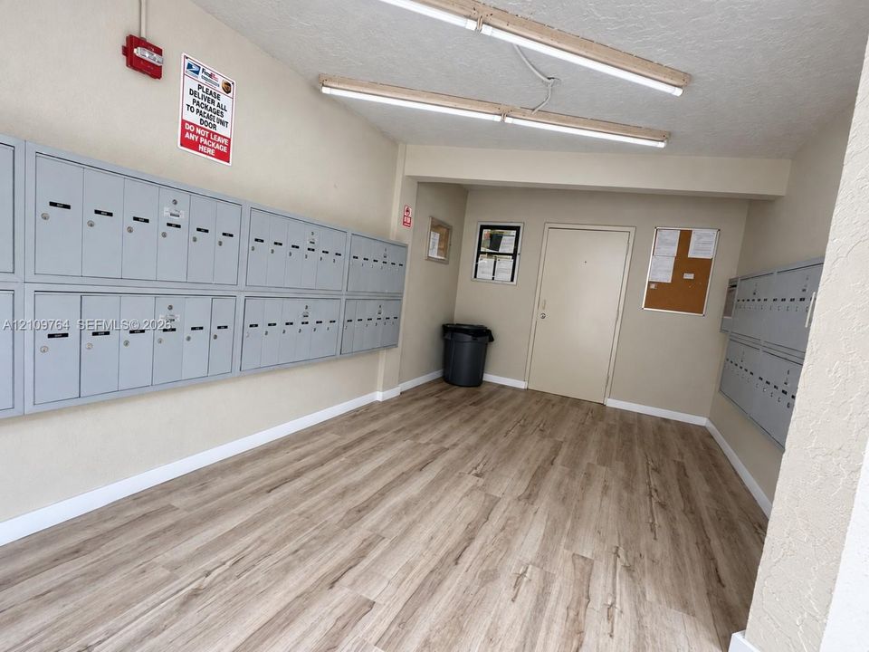 Dedicated mail room featuring wall-mounted metal mailboxes, wood-finish flooring, and overhead lighting