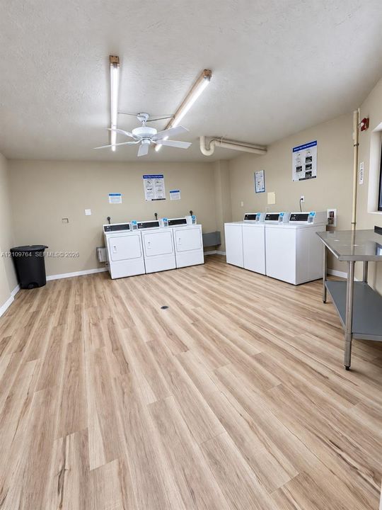 Laundry room featuring wood-finish flooring, linear lighting, a ceiling fan, and multiple built-in laundry appliances
