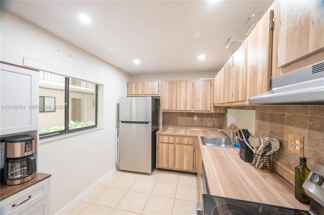 Kitchen featuring wood cabinetry, stainless steel refrigerator, stone-style backsplash, integrated countertop, and ceramic tile flooring