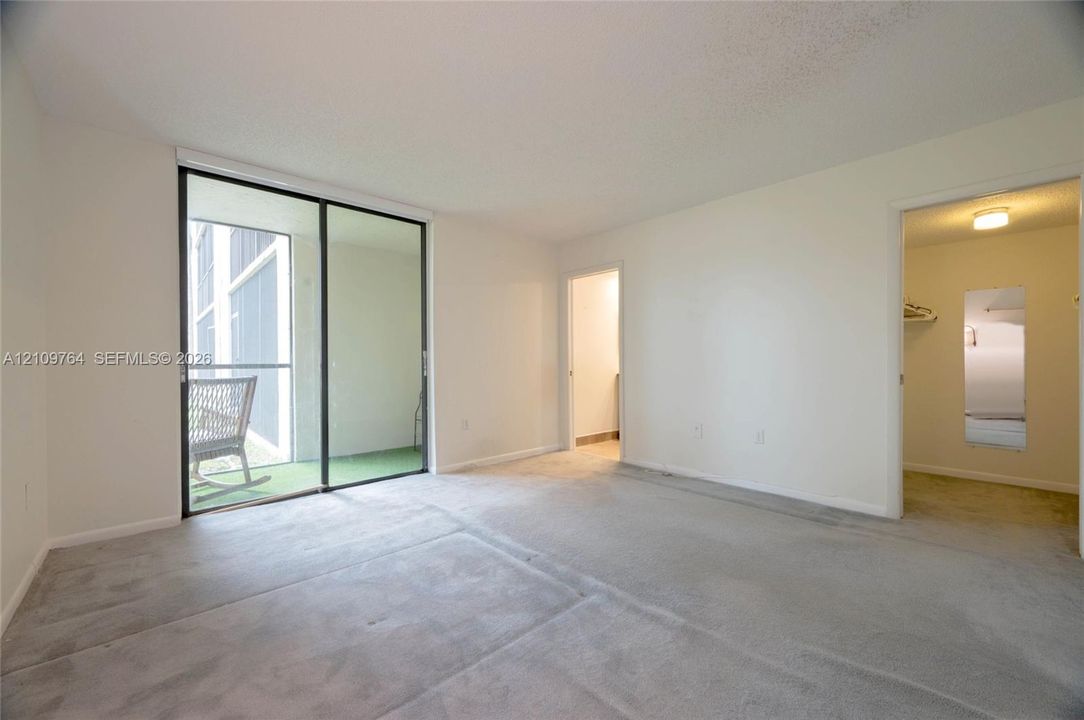Large primary br with bath & walk-in closet, featuring sliding doors to screened balcony, neutral grey carpeting