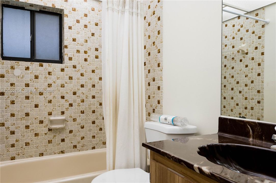 guest Bathroom featuring a patterned mosaic tile shower surround, integrated bathtub, dark stone-surface vanity with an oval undermount sink, and a large wall-mounted mirror