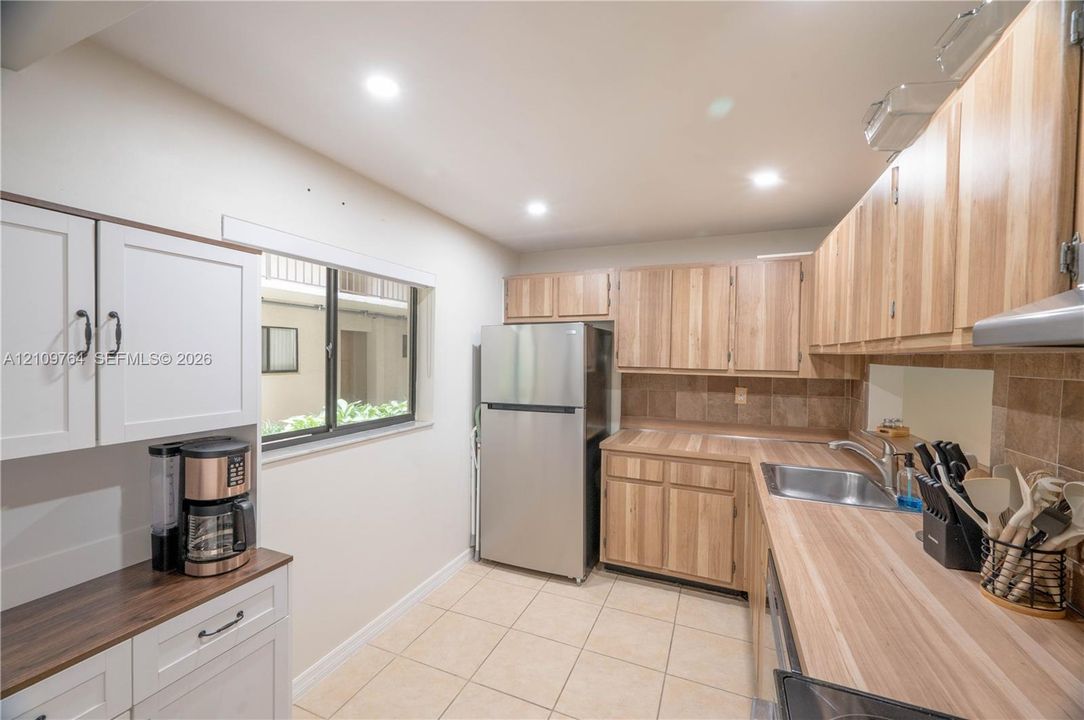 Kitchen featuring wood cabinetry, laminate countertops, a stainless steel refrigerator, tile backsplash, and ceramic tile flooring