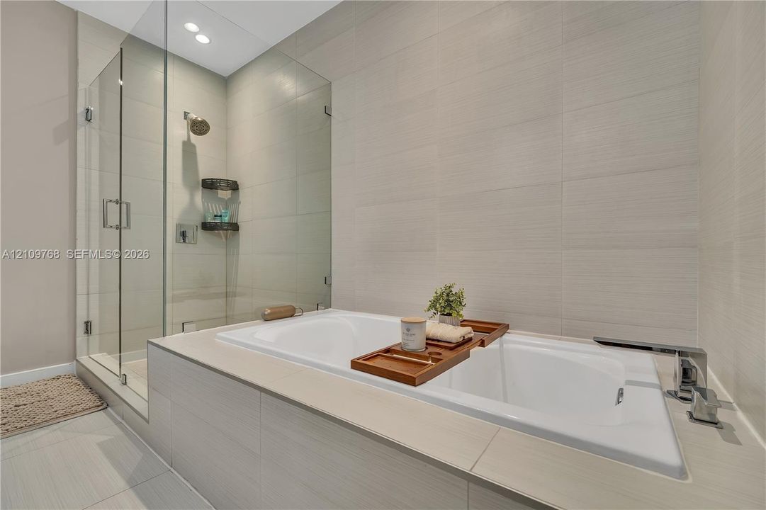 Soaking tub with a deck-mounted faucet, walk-in glass shower enclosure, and large-format tile surround