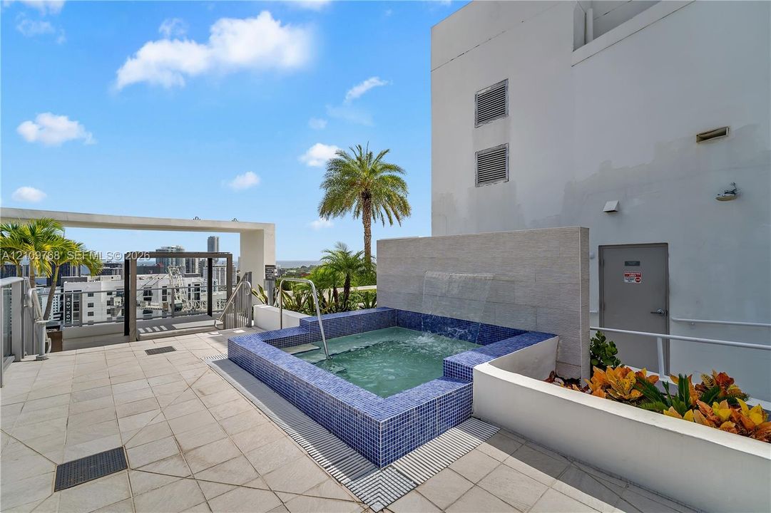Rooftop terrace featuring a tiled spa with a cascading water feature, stone accent wall, paved deck, and metal pergola structure