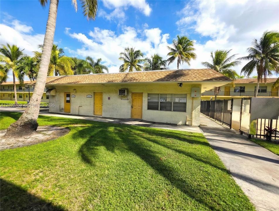 Single-story exterior featuring a shingled roof, stucco finish, exterior-entry doors, and mature palm trees situated on a grassy landscape