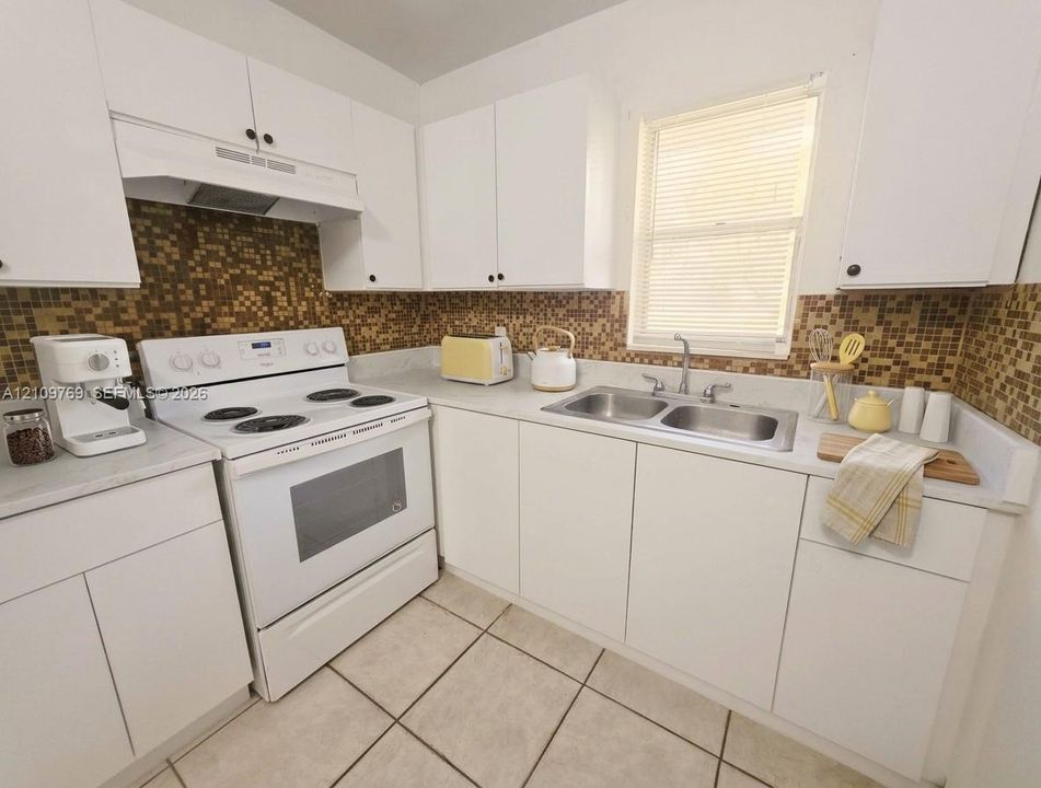 Kitchen featuring white cabinetry, mosaic tile backsplash, electric range with overhead vent hood, dual-basin stainless steel sink, and ceramic tile flooring