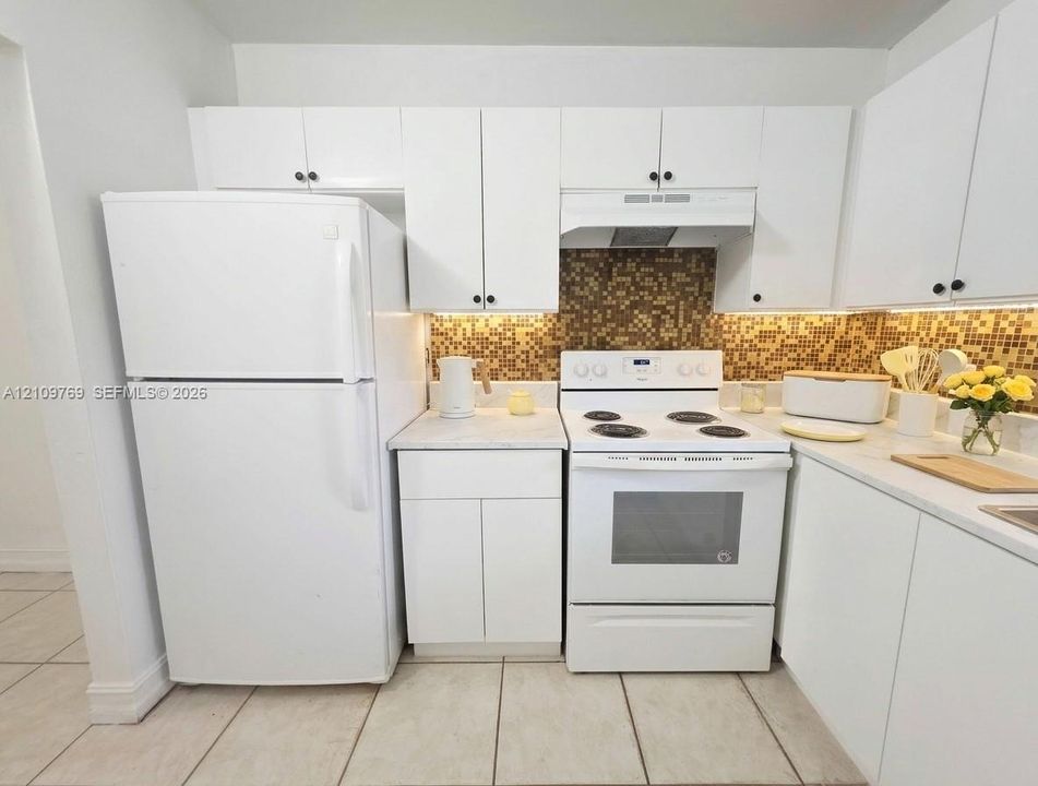Kitchen featuring white cabinetry, solid-surface countertops, a tiled mosaic backsplash, an integrated range hood, and tile flooring