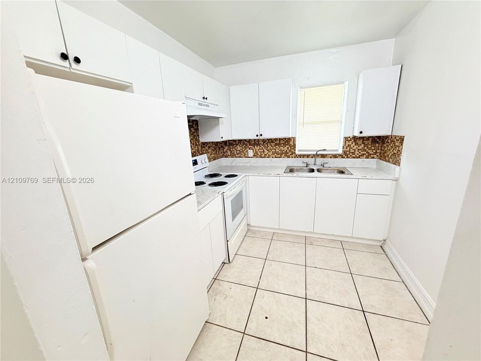 Kitchen featuring white cabinetry, light-toned stone-finish countertops, decorative mosaic tile backsplash, double-basin stainless steel sink, and ceramic tile flooring