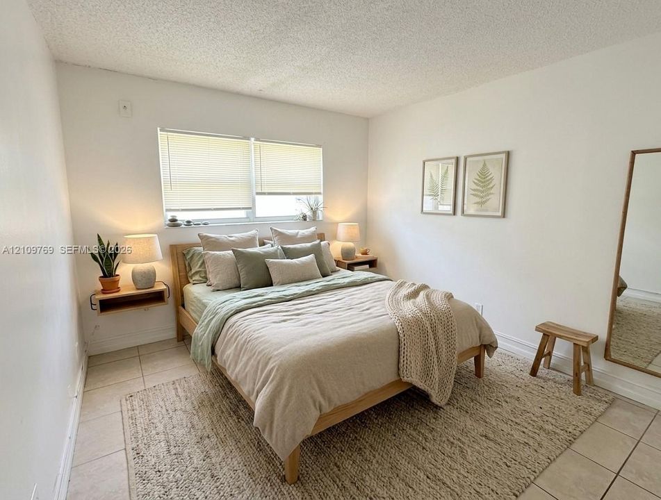 Neutral interior featuring ceramic tile flooring, a horizontal sliding window with blinds, and a built-in wall-mounted shelving unit