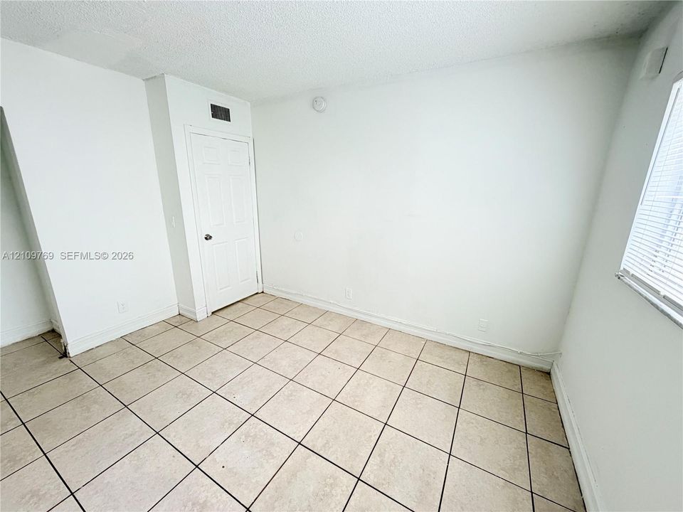 Interior space featuring neutral tile flooring, a six-panel door, and a multi-pane window with integrated blinds