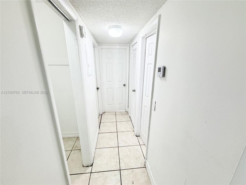 Hallway featuring large-format square tile flooring, white six-panel interior doors, and a flush-mount ceiling light fixture