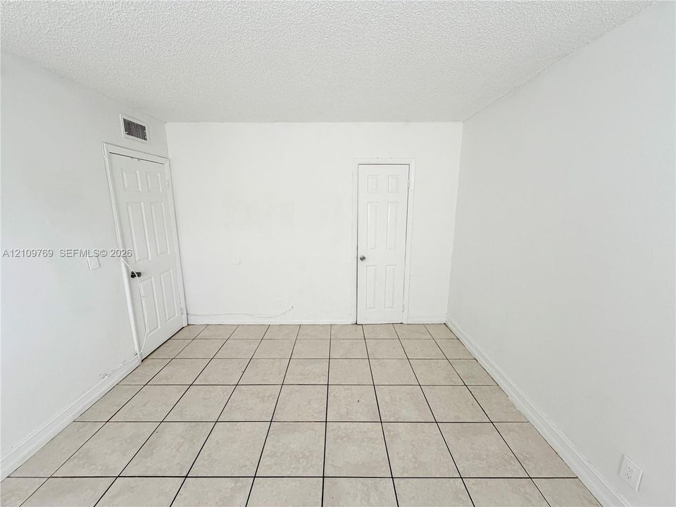 Neutral interior space featuring ceramic tile flooring, textured ceiling finish, and two six-panel doors