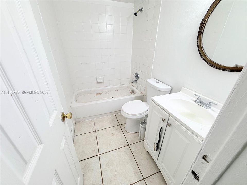 Bathroom featuring a white vanity with an integrated sink, porcelain tile flooring, and a bathtub with tile surround