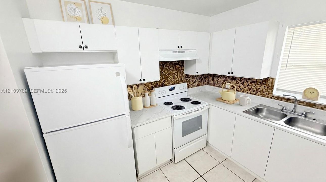 Kitchen featuring white cabinetry, light-toned countertops, a mosaic tile backsplash, a white range, and a double-basin stainless steel sink