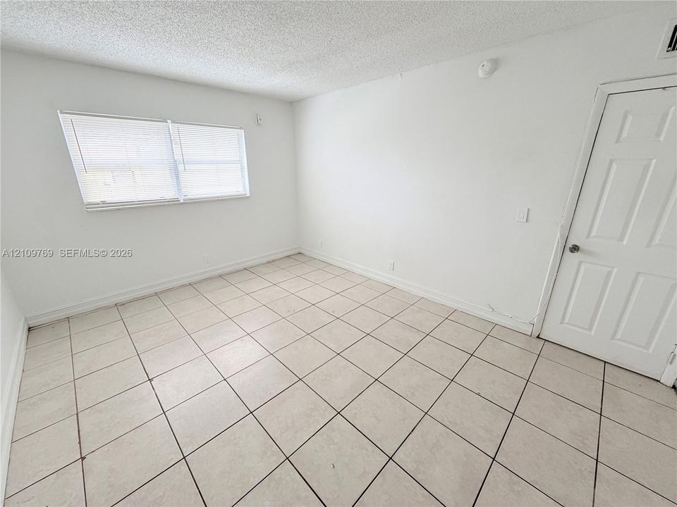 Neutral-toned ceramic tile flooring, solid-core interior door, and window with integrated blinds