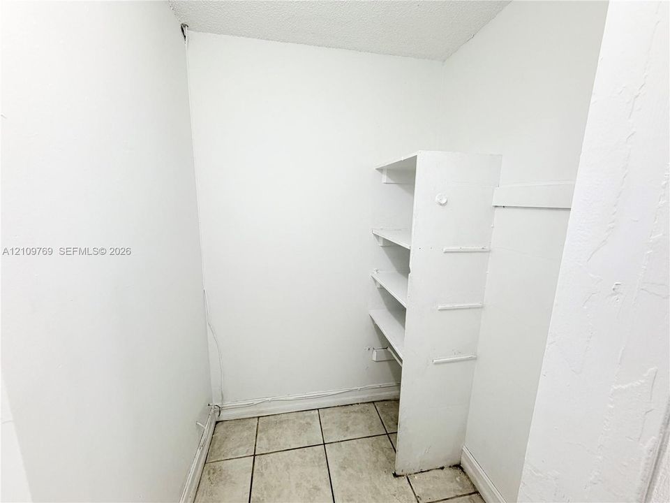 Storage area featuring neutral tile flooring and built-in white shelving