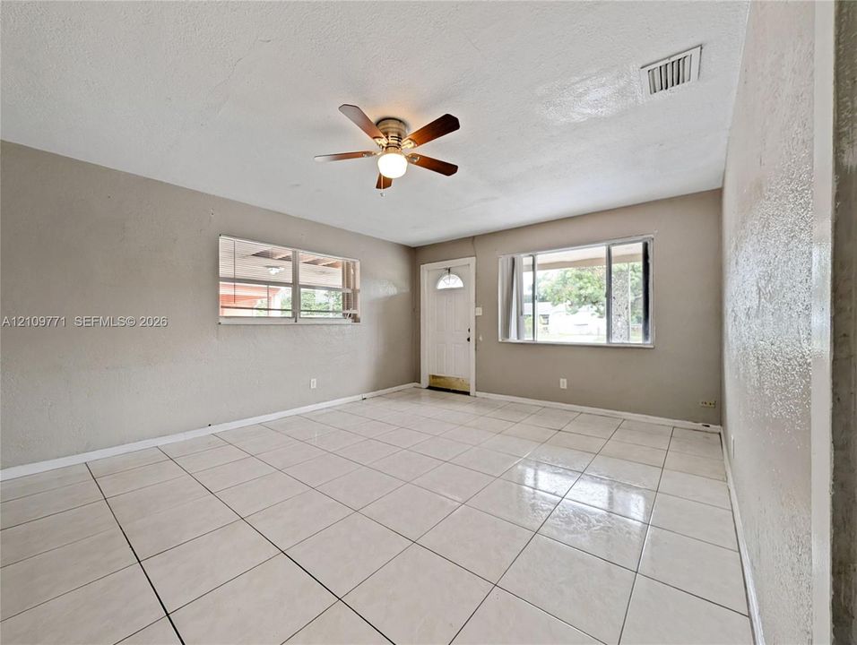 Interior space featuring large-format tile flooring, a central ceiling fan with integrated lighting, neutral wall paint, and windows with multi-pane horizontal sliders