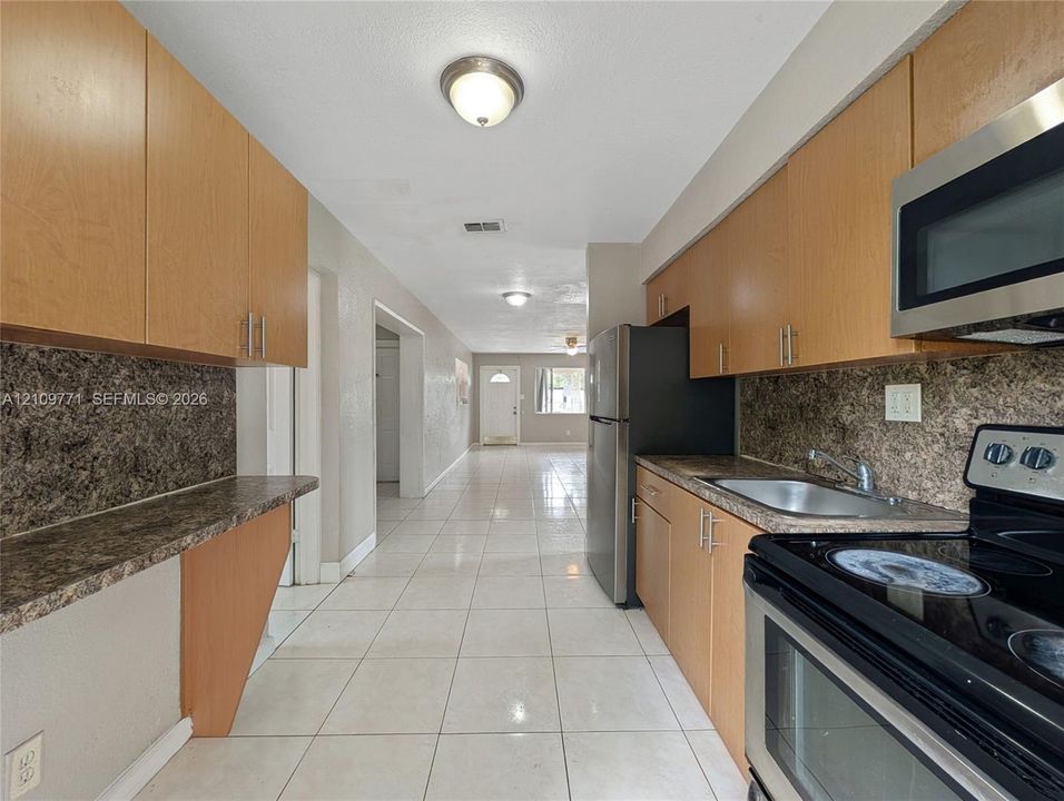 Kitchen featuring light wood-finish cabinetry, patterned stone-finish countertops, tile flooring, stainless steel appliances, and flush-mount lighting