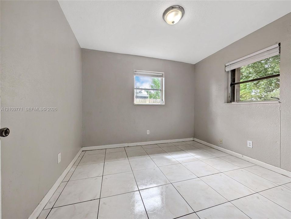 Neutral-toned interior room featuring large-format ceramic tile flooring, two windows with blinds, and a flush-mount ceiling light fixture