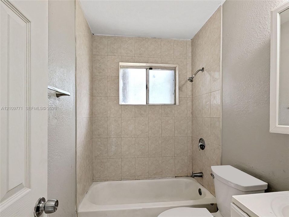 Bathtub enclosure featuring full-height ceramic wall tile, a sliding window, a metal showerhead, and a wall-mounted faucet