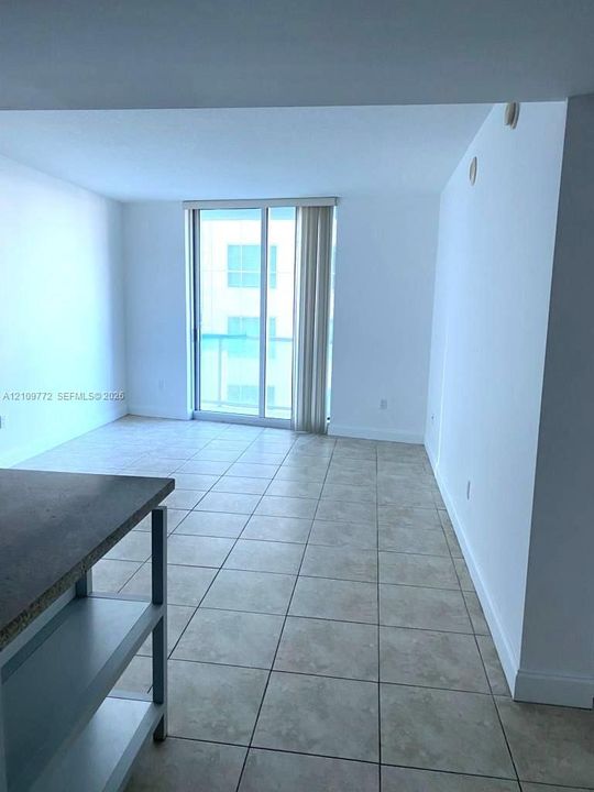 Open-concept interior featuring neutral tile flooring, sliding glass doors, and a built-in kitchen island with a stone-finish countertop