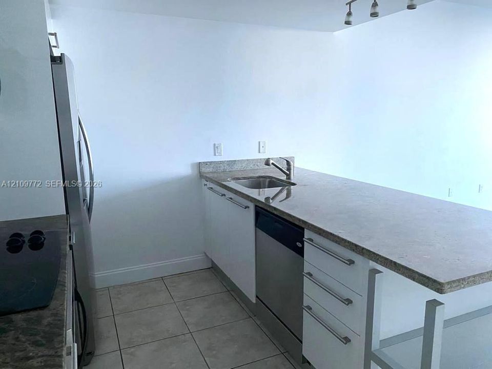Kitchen featuring stone-finish countertops, stainless steel undermount sink, built-in dishwasher, white cabinetry with horizontal hardware, and tile flooring
