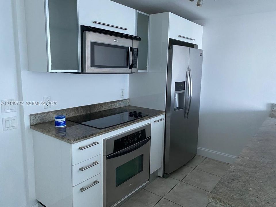Kitchen featuring white flat-panel cabinetry, stone countertops, stainless steel appliances, and ceramic tile flooring