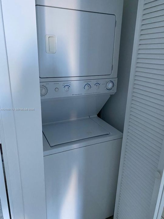 Stacked laundry unit featuring a top-load washer, front-load dryer, and louvered closet doors