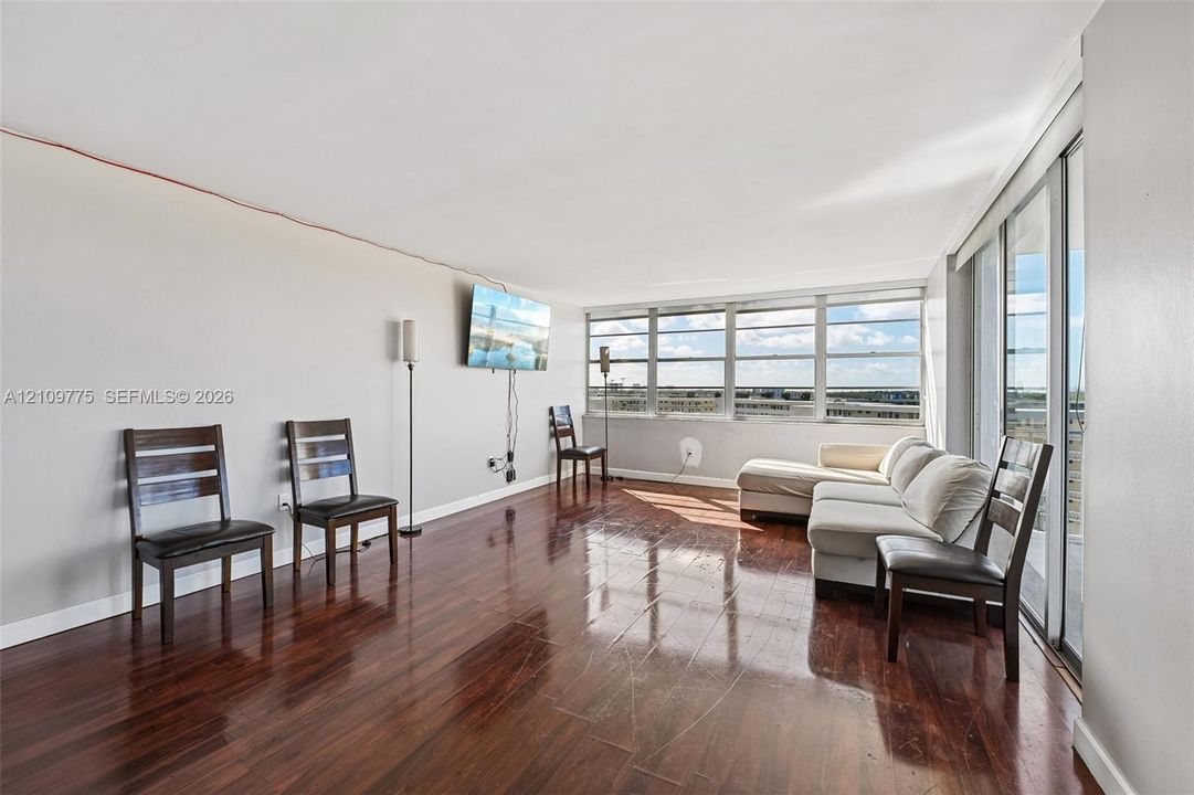 Spacious living area featuring polished wood-finish flooring, floor-to-ceiling windows, and sliding glass balcony doors