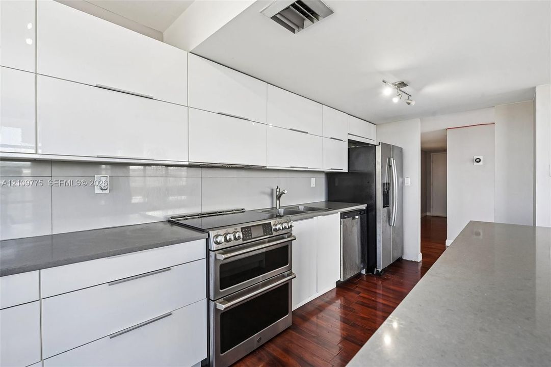 Kitchen featuring white high-gloss slab cabinetry, dark solid-surface countertops, stainless steel appliances, and dark-stained hardwood flooring