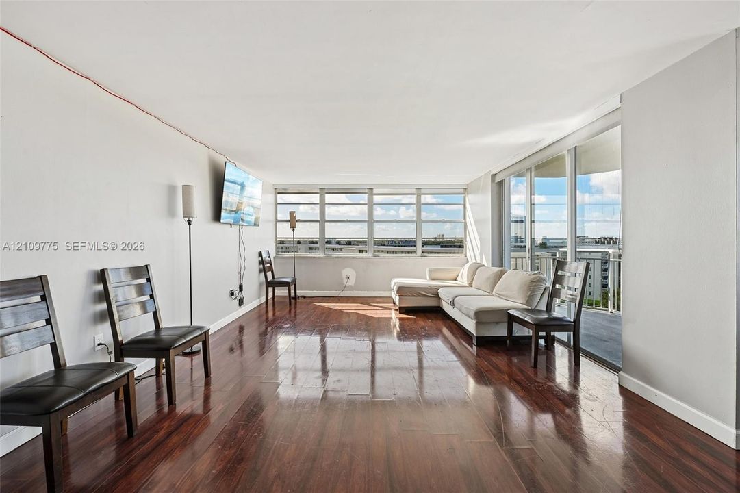 Expansive living area featuring wood-finish flooring, floor-to-ceiling windows, and a sliding glass door providing access to a balcony