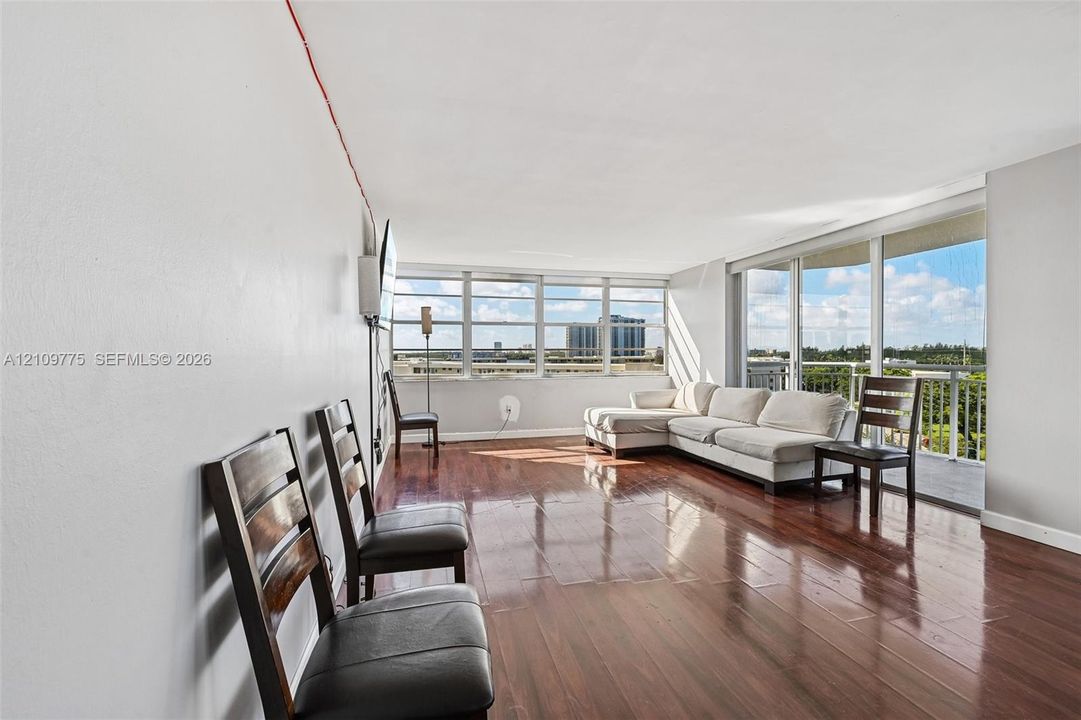 Living area featuring wood-finish flooring, floor-to-ceiling windows, and a sliding glass door providing access to a private balcony