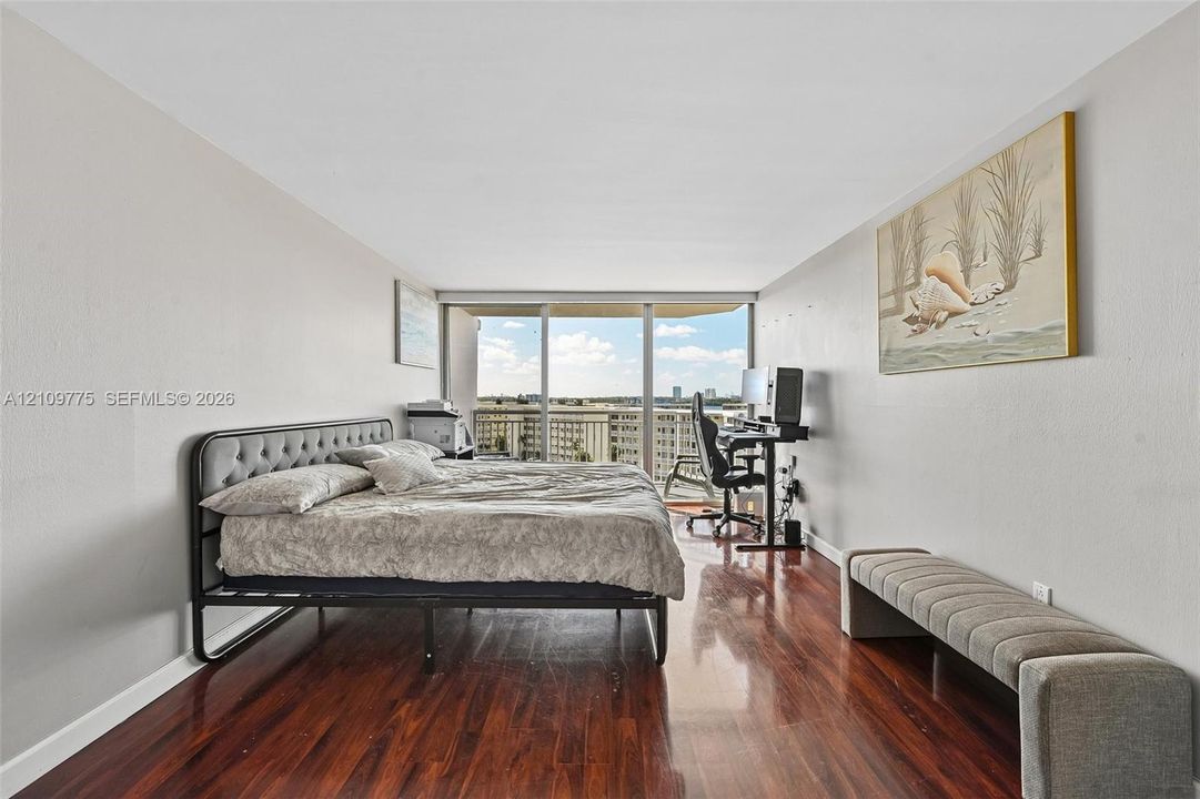 Wood-finish flooring, neutral wall tones, and floor-to-ceiling glass sliding doors opening to an exterior balcony
