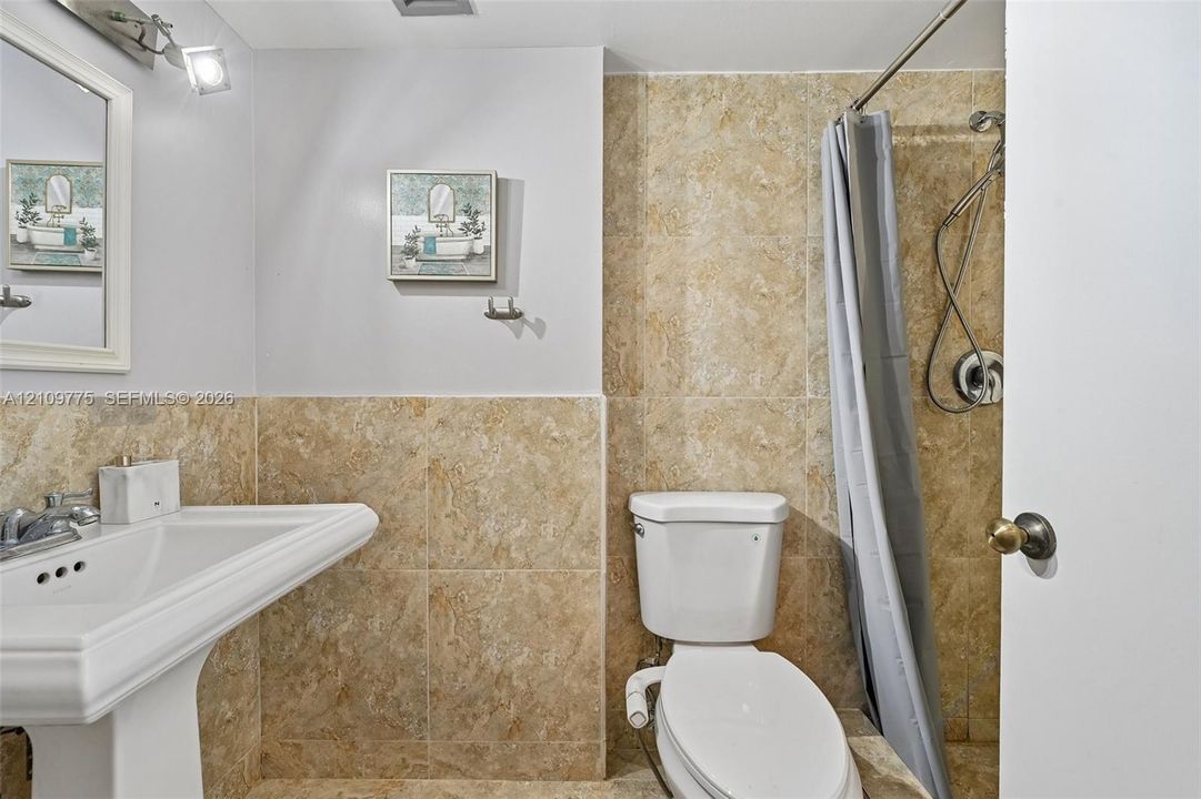 Pedestal sink with chrome faucet, wall-mounted vanity mirror, and floor-to-ceiling neutral-toned tile shower enclosure