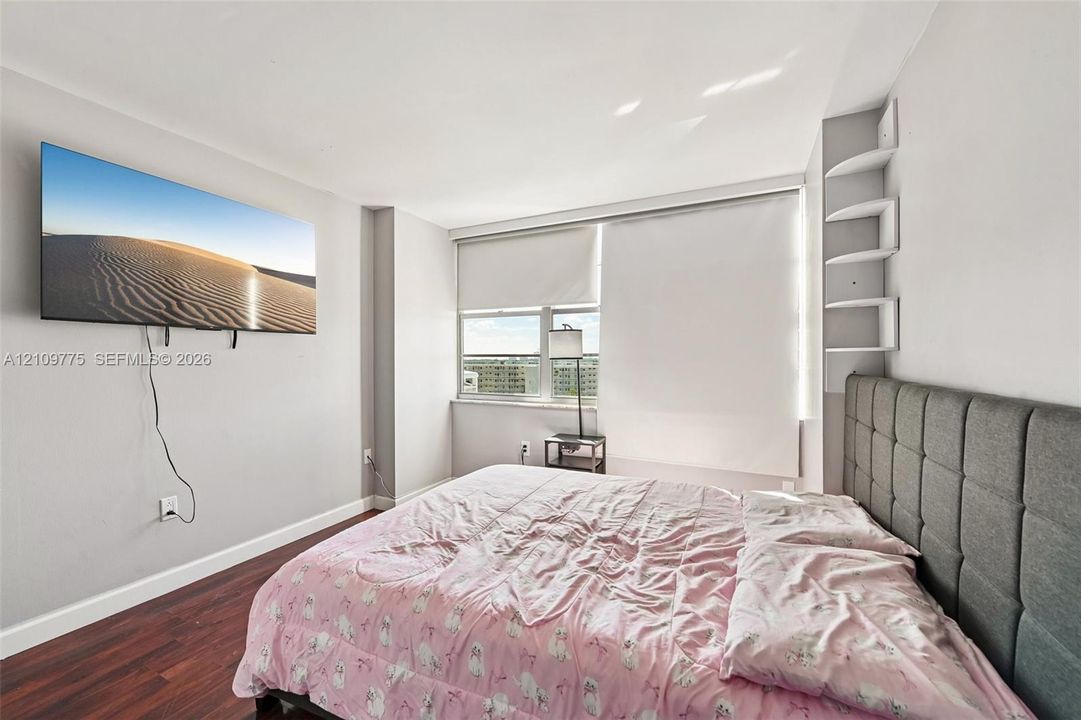 Room featuring wood-finish flooring, multi-pane window with integrated roller shades, and built-in corner shelving