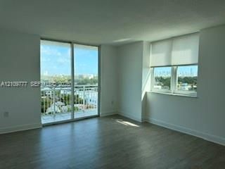 Interior space featuring wood-finish flooring, floor-to-ceiling sliding glass doors opening to a balcony, and expansive windows with roller shades