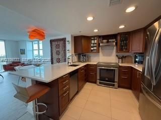 Kitchen featuring wood cabinetry, stone countertops, stainless steel appliances, tile flooring, and recessed ceiling lighting
